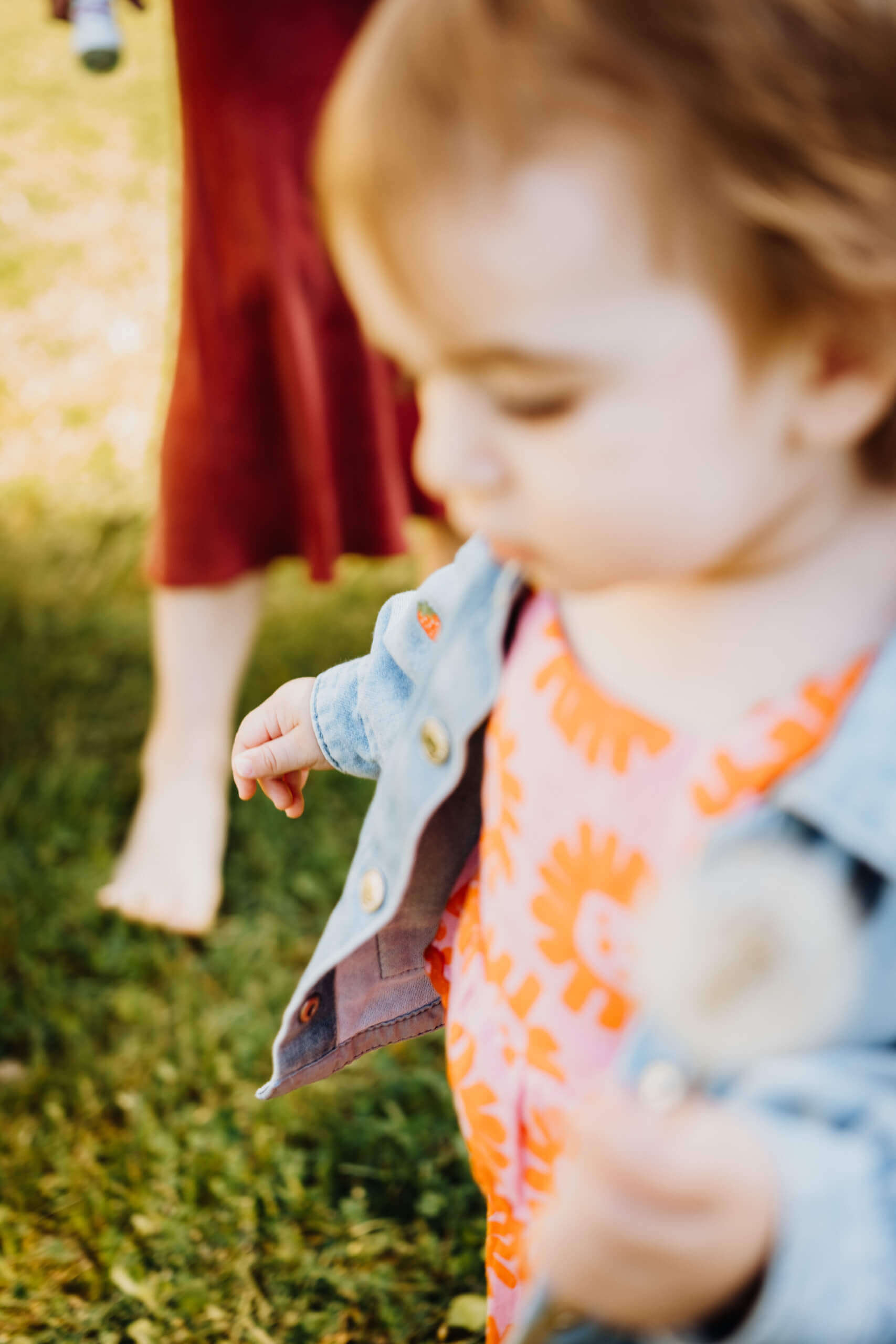 Kleines Mädchen im Jeansjacke mit Blumenmuster-Kleid, Elternteil im Hintergrund