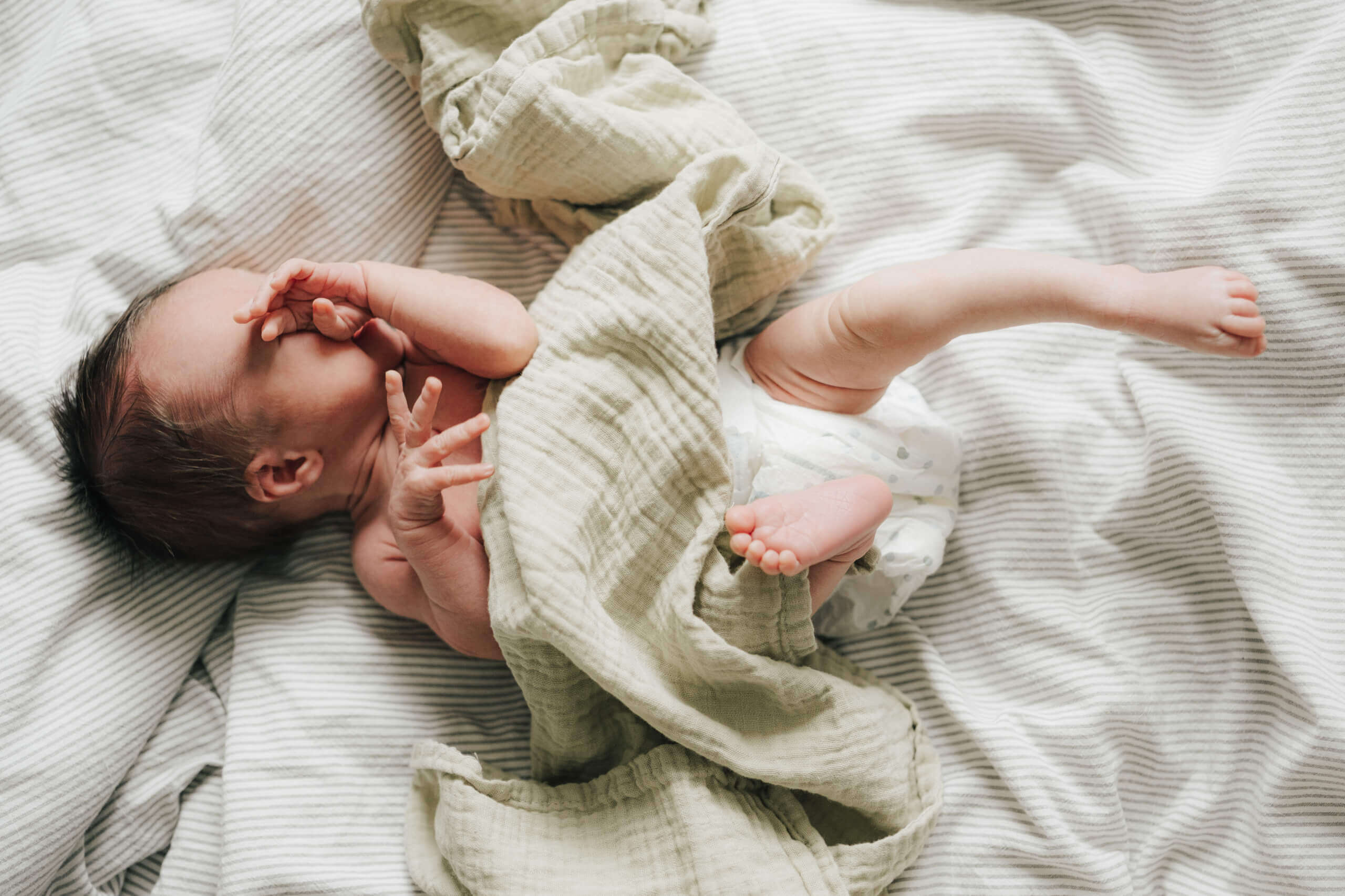 Neugeborenes Baby liegt auf einer gestreiften Decke, bedeckt mit einem leichten Tuch.