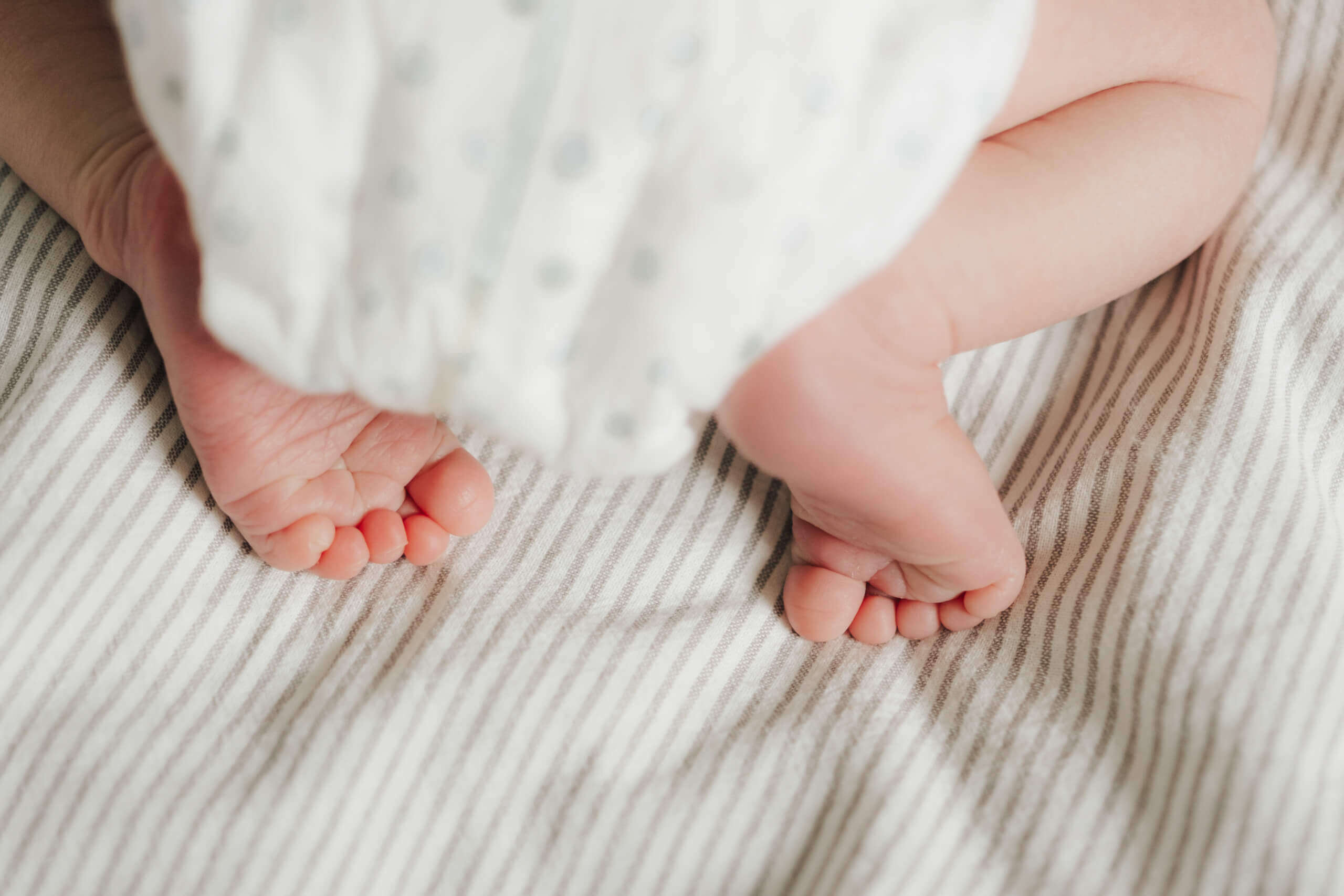 Neugeborenenfüße auf gestreifter Decke, Fokus auf zarte Zehen