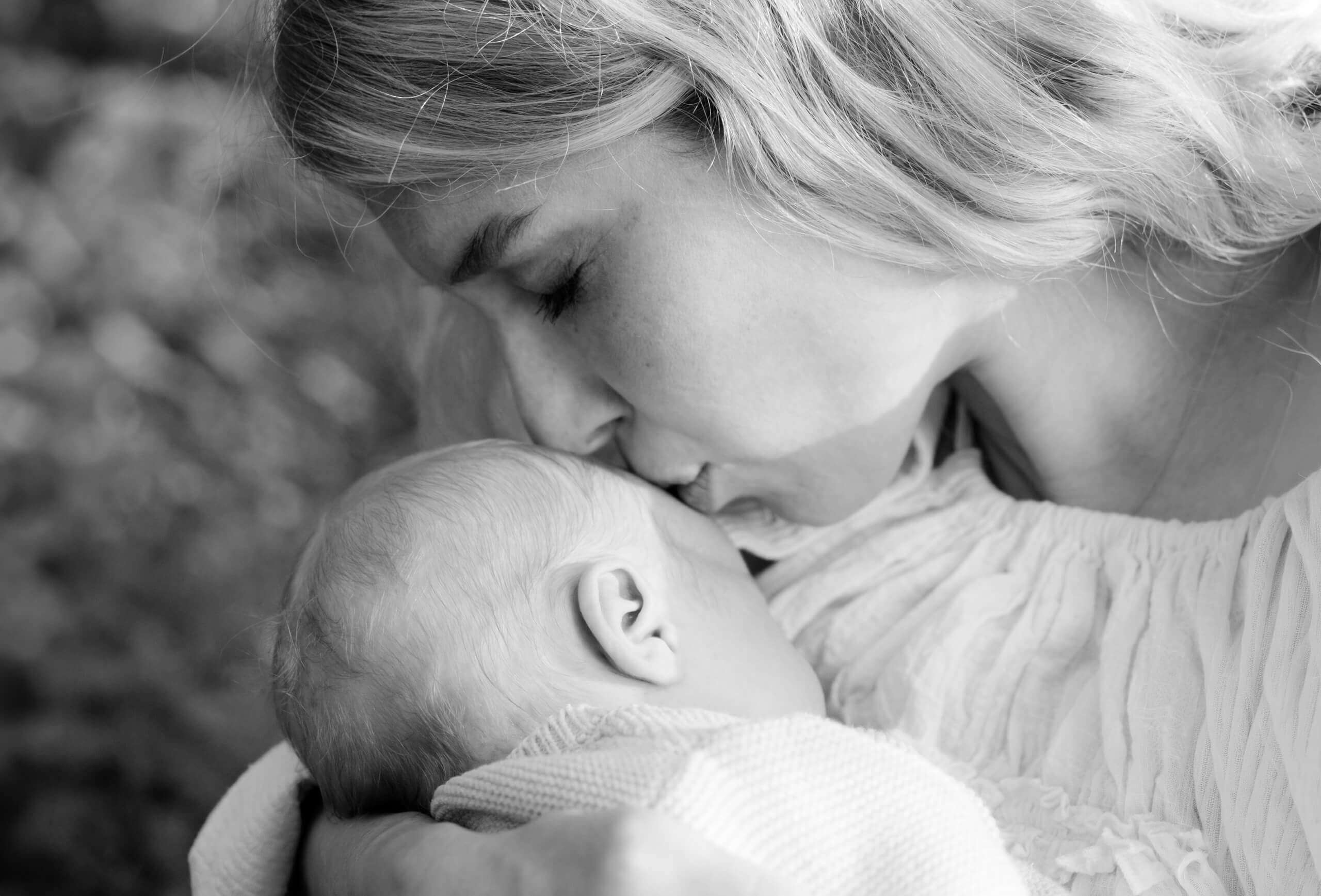 Mutter küsst ihr schlafendes Neugeborenes – Newbornfotos
